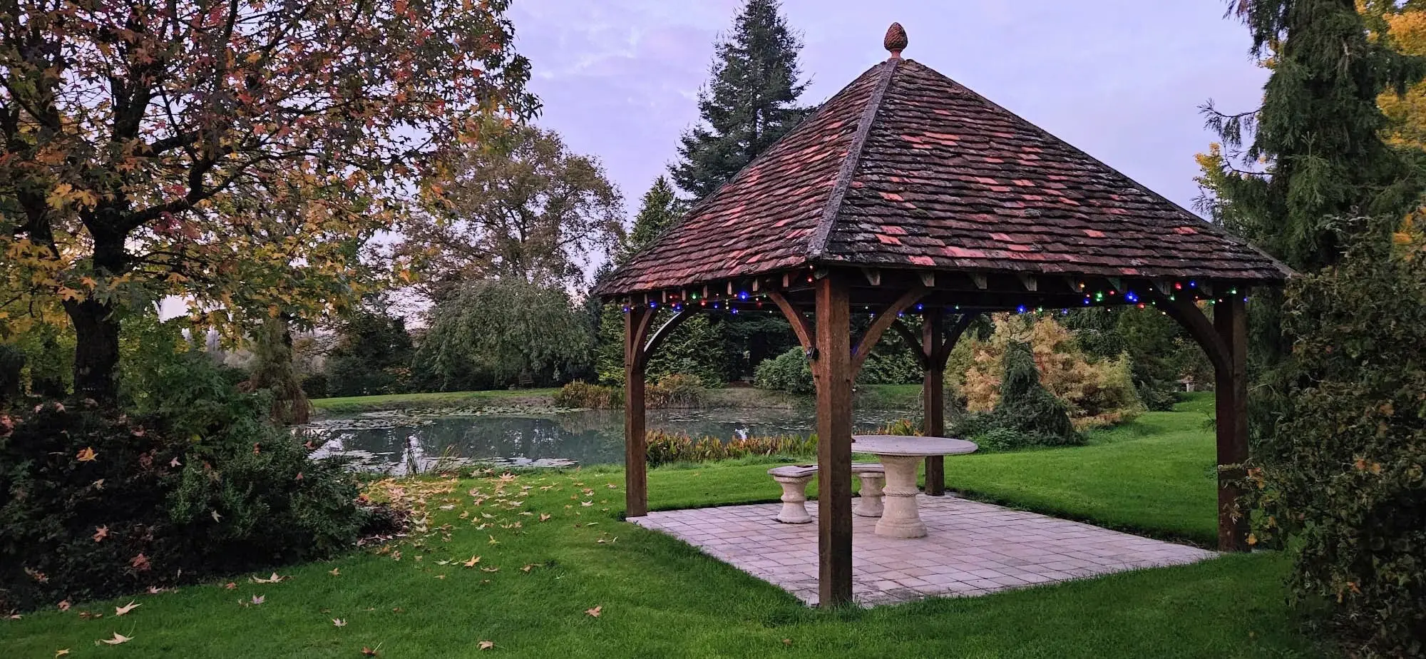 Gloriette hexagonale en bois, au bord du plan d'eau, sous un ciel de fin de journée